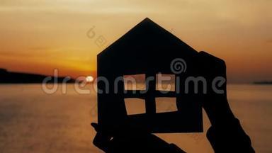 <strong>剪影</strong>一个用纸板做的小纸屋，在海上日落时用手握住。 效率及<strong>家居</strong>概念-